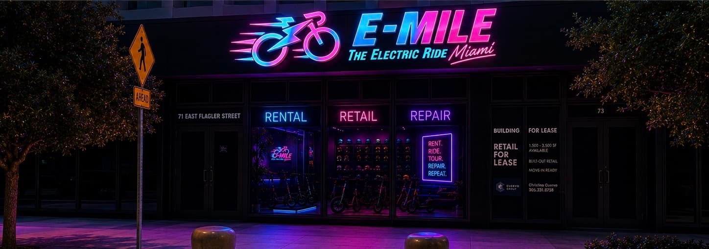 Vibrant pink and blue neon signs illuminate the E-MILE electric bike shop storefront at night.